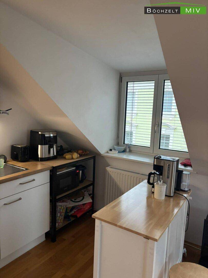 Helle Dachgeschossküche mit Fenster, Holztheke und Kaffeemaschine, bietet eine gemütliche Kochumgebung.