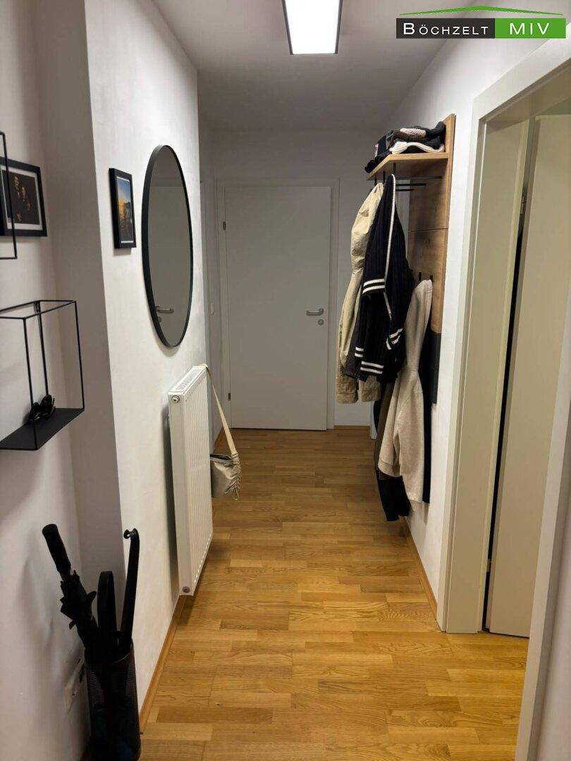 Heller Flur mit Holzboden, Garderobe und Spiegel, bietet praktischen Stauraum und eine einladende Atmosphäre.