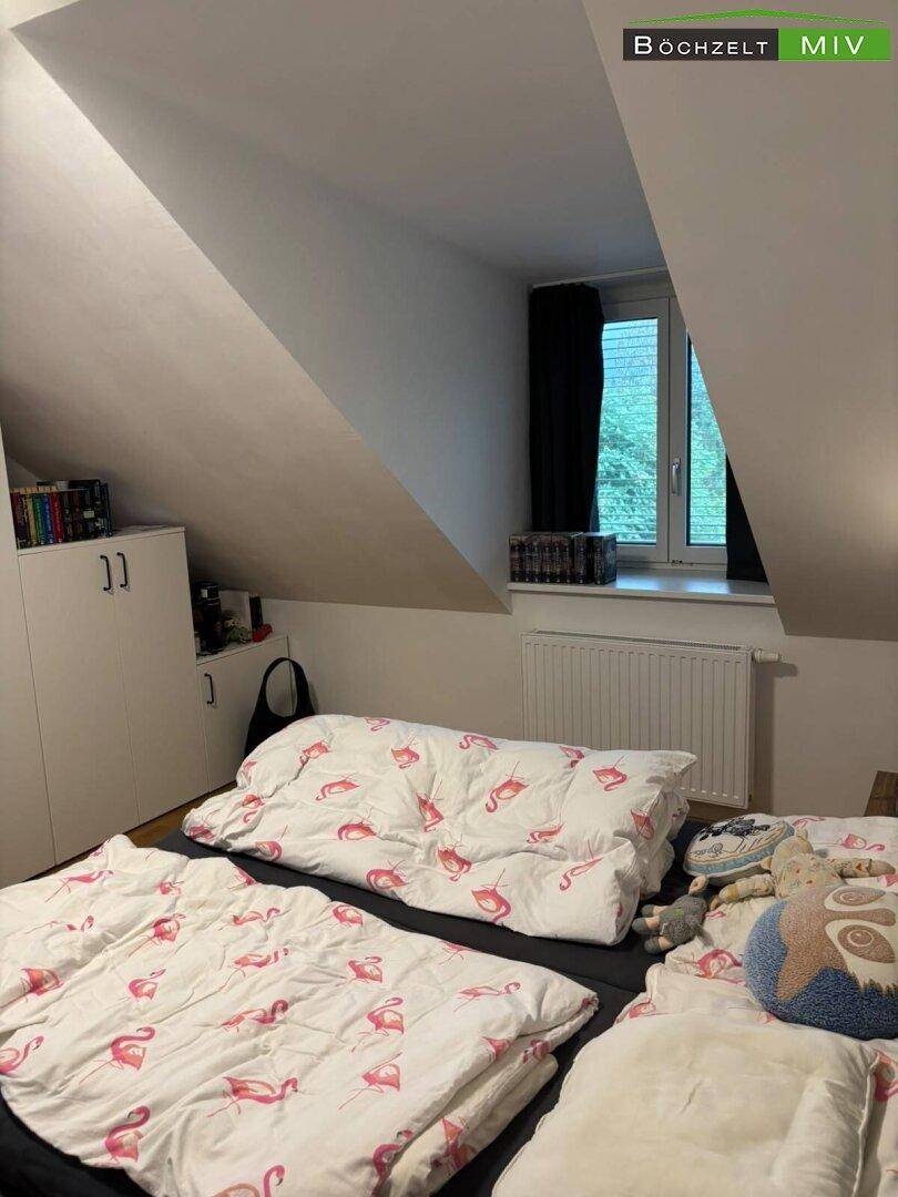 Helles Schlafzimmer im Dachgeschoss mit Fenster und Holzboden, ideal für erholsamen Schlaf.
