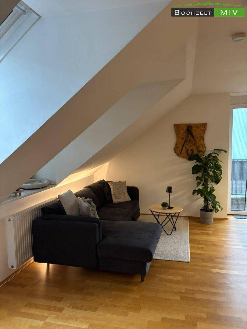 Gemütliches Wohnzimmer im Dachgeschoss mit Sofa, Holzboden und schrägen Wänden, bietet eine entspannte Atmosphäre.