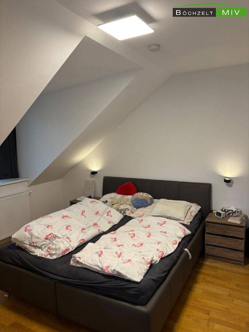Schlafzimmer im Dachgeschoss mit Doppelbett, Holzboden und schrägen Wänden, bietet eine ruhige Rückzugsmöglichkeit.