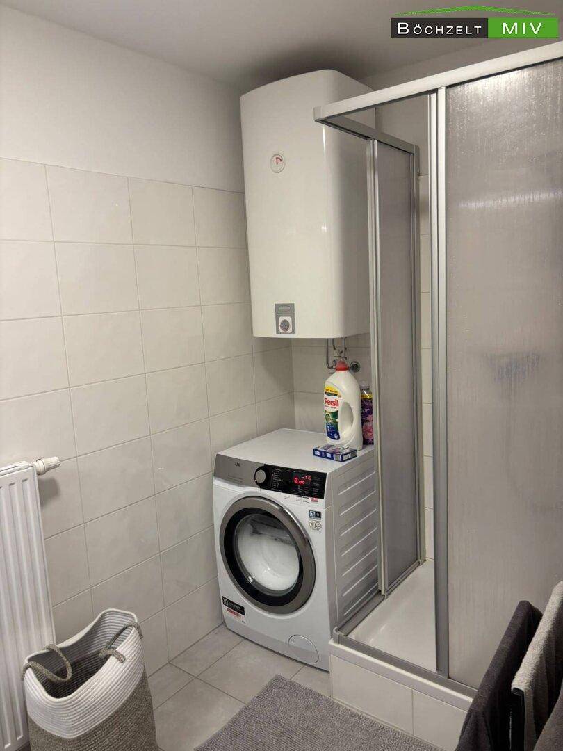 Badezimmer mit Dusche und Waschmaschine, hell gefliest und praktisch eingerichtet für den Alltag.