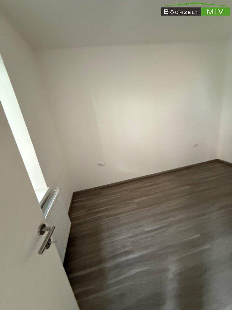 Leeres Zimmer mit hellem Laminatboden und weiß gestrichenen Wänden, bereit zum Einzug.