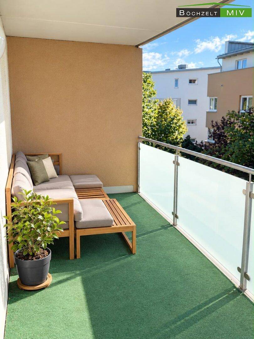 Gemütlicher Balkon mit Sitzgelegenheiten, Glasbrüstung und Blick auf die Umgebung.