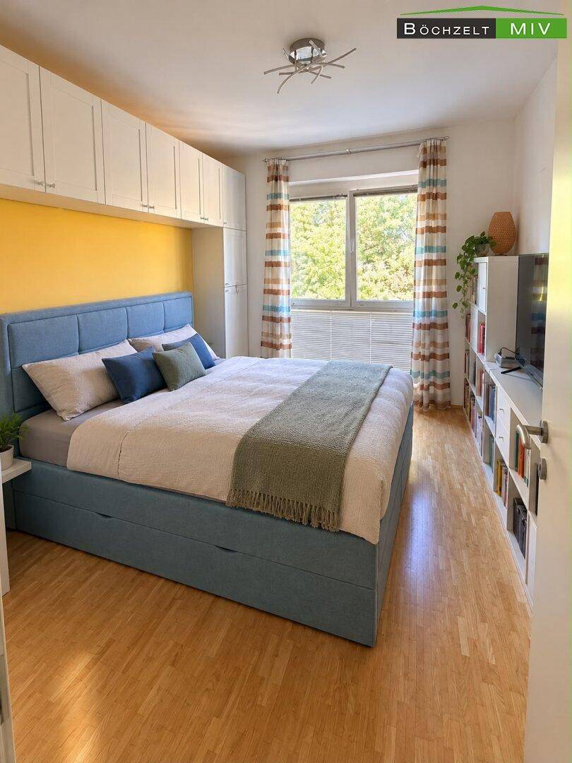 Gemütliches Schlafzimmer mit blauem Bett, gelber Akzentwand und Einbauschränken über dem Bett.