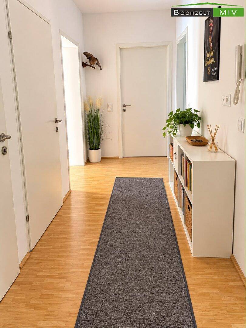 Heller Flur mit Holzboden, weißen Türen und einem schmalen Regal für Dekoration.