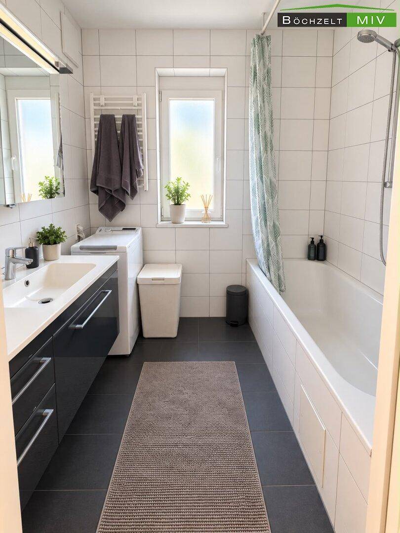 Modernes Badezimmer mit Badewanne, Waschbecken, dunklen Fliesen und Fenster für Tageslicht.