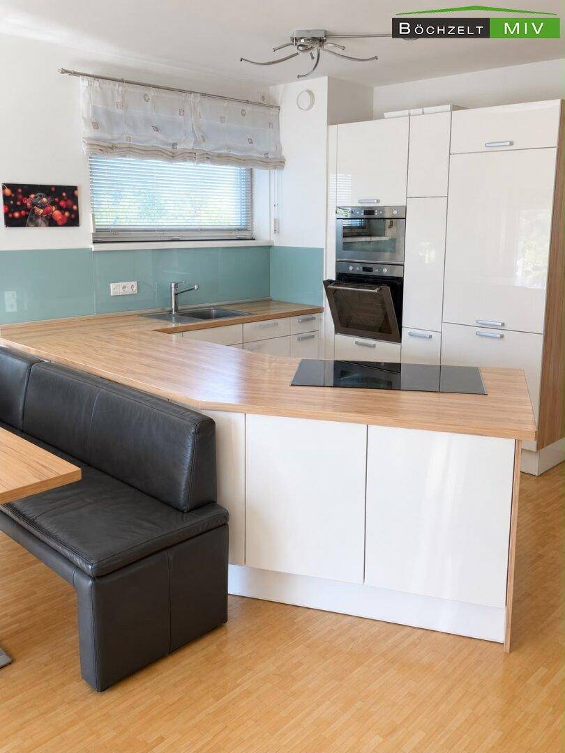 Moderne Einbauküche mit Holztheke, integriertem Essbereich und weißen Hochglanzfronten.