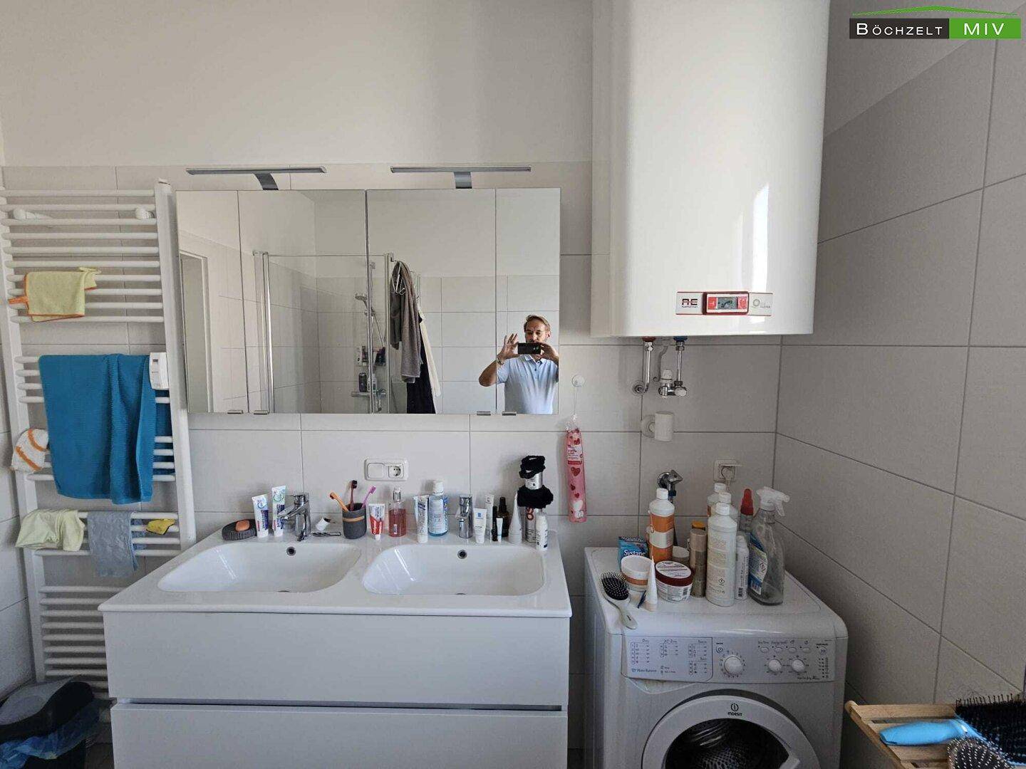 Modernes Badezimmer mit Doppelwaschbecken, Waschmaschine und Wandspiegel.