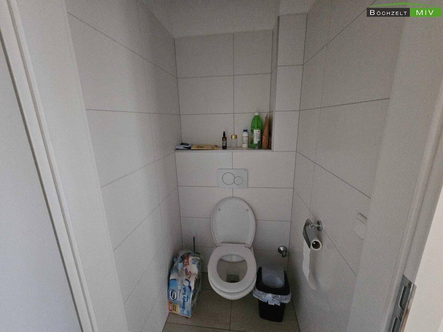 Separates WC mit Wandtoilette und hellen Fliesen an Wänden und Boden.