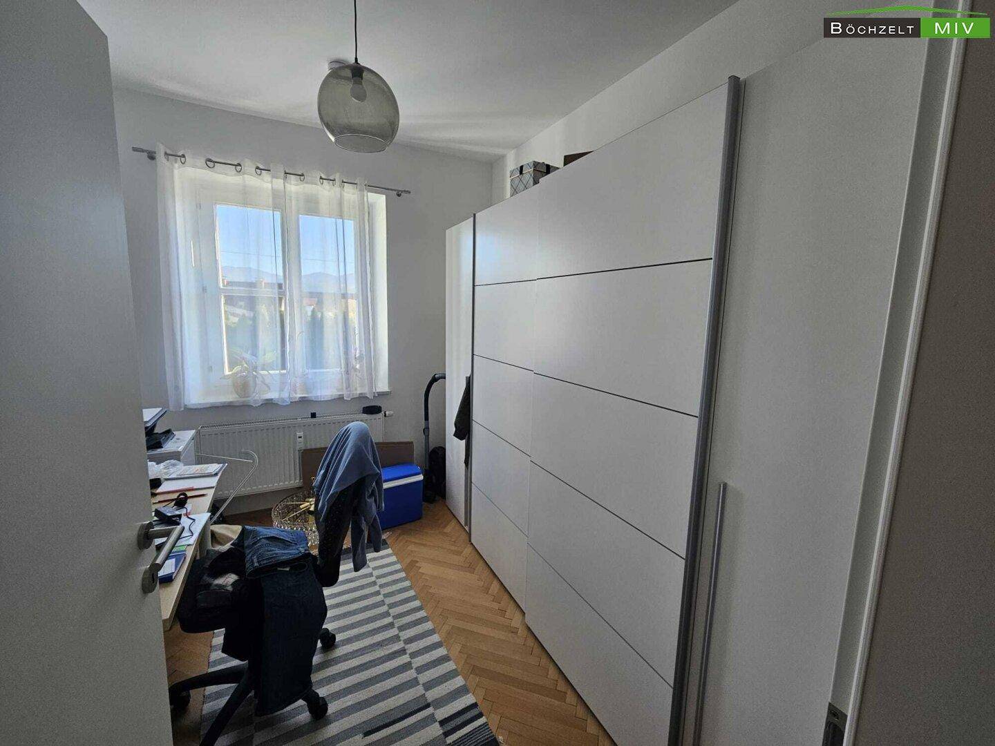 Helles Arbeitszimmer mit großem Kleiderschrank, Schreibtisch und Fensterblick.