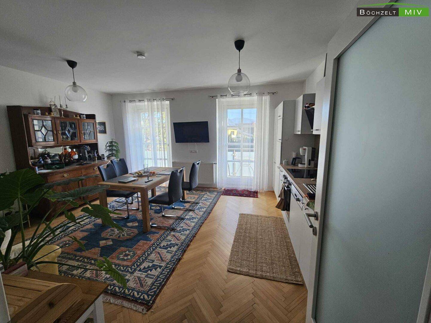 Heller Wohn- und Essbereich mit Fischgrätparkett, Esstisch und Zugang zu einem Balkon.