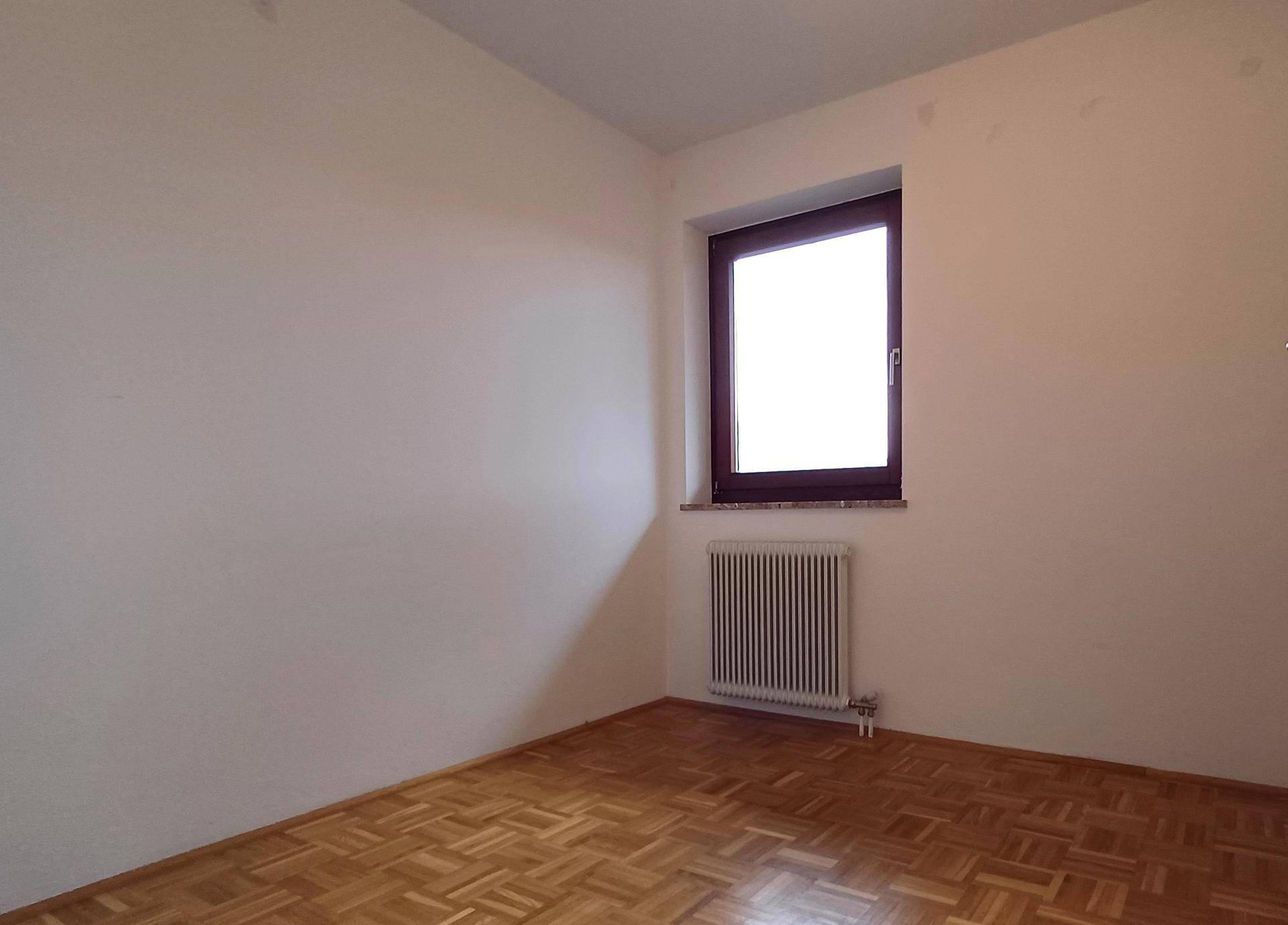 Helles Schlafzimmer mit Parkettboden, weiß gestrichenen Wänden und einem Fenster.