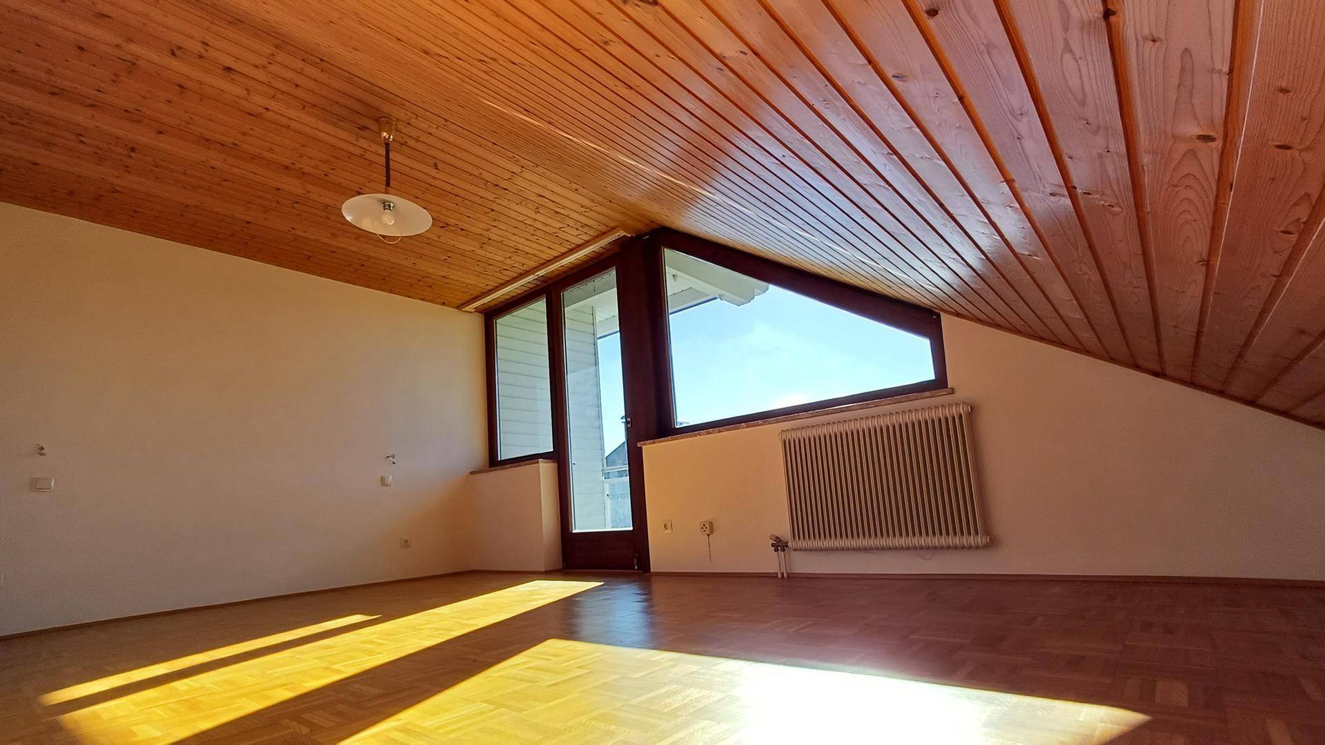 Dachgeschosszimmer mit Holzdecke, Parkettboden und großen Fenstern für viel Licht.