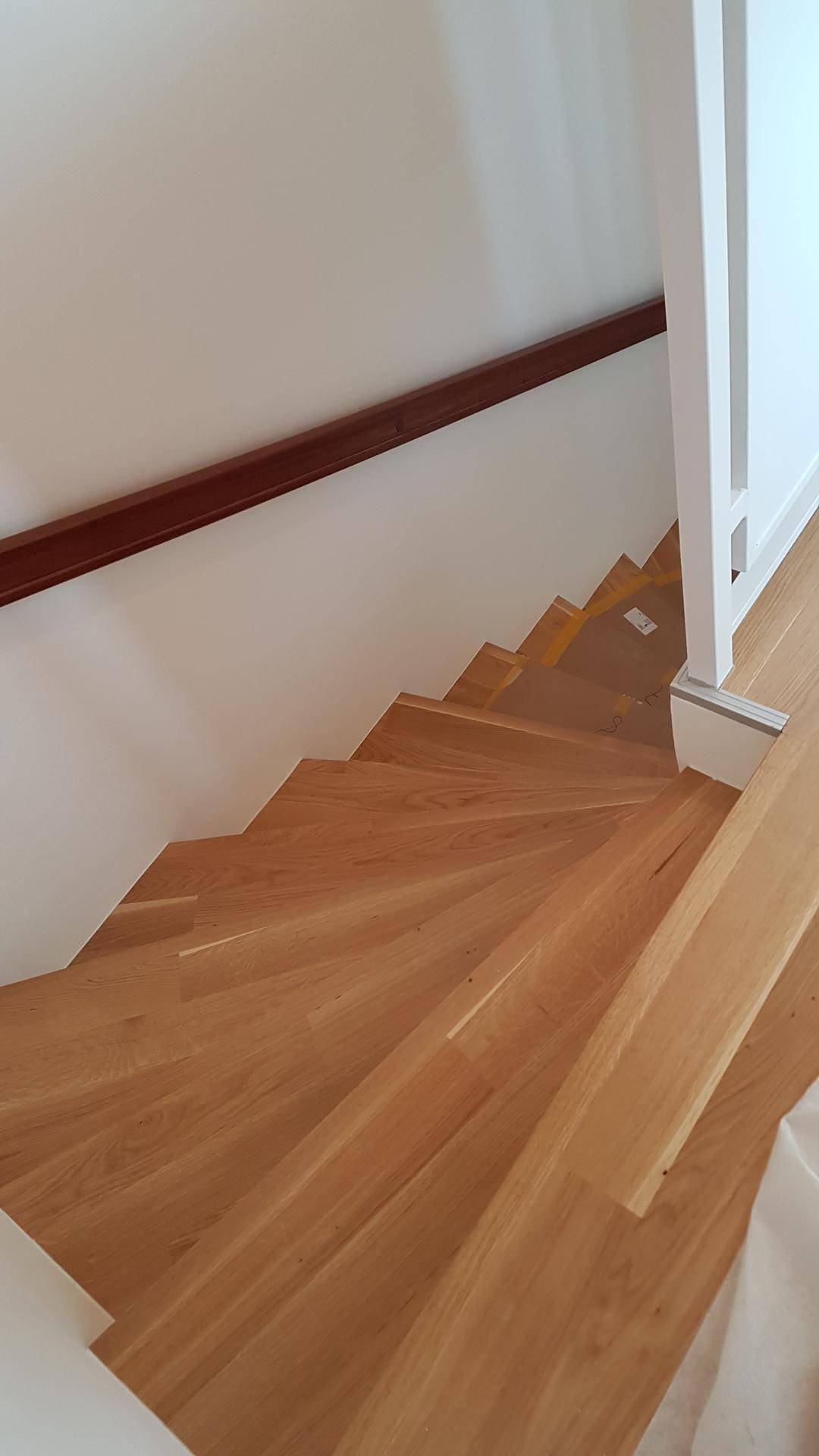 Holztreppe mit hellem Geländer, die die verschiedenen Etagen des Hauses verbindet.