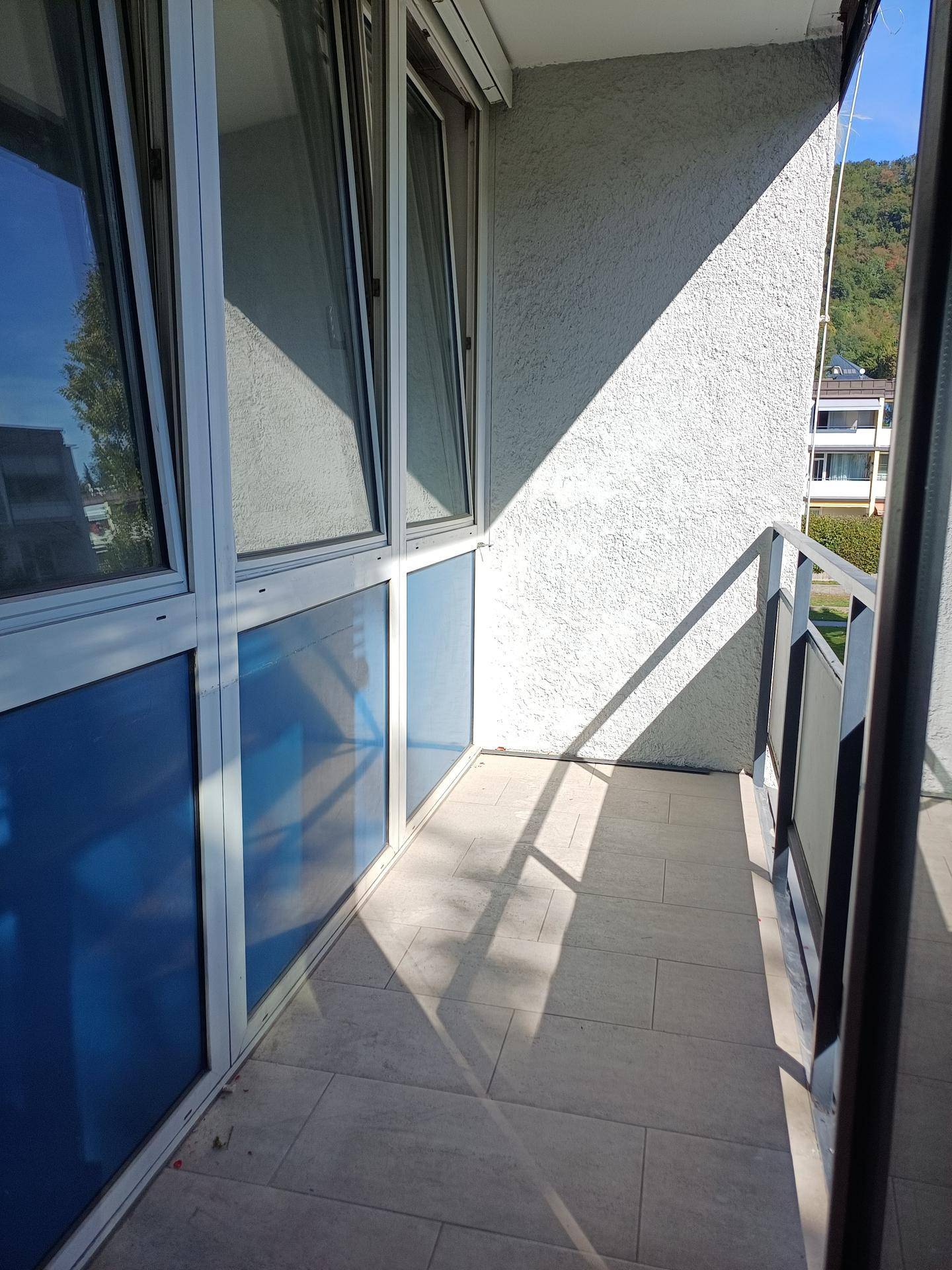 Heller Balkon mit Fliesenboden und blauen Glaselementen, der viel Sonnenlicht einfängt.