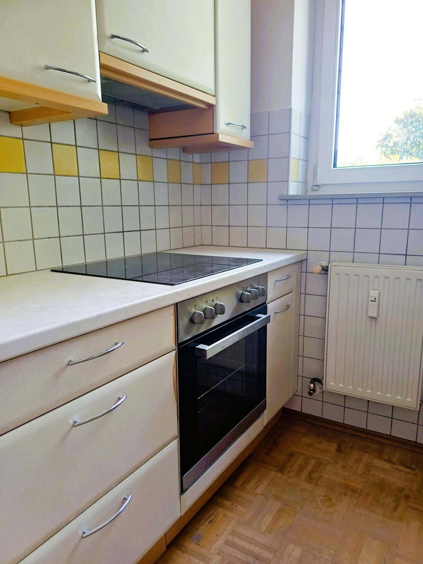 Küche mit Einbauherd, Kochfeld und gelb-weißen Fliesen an der Wand.