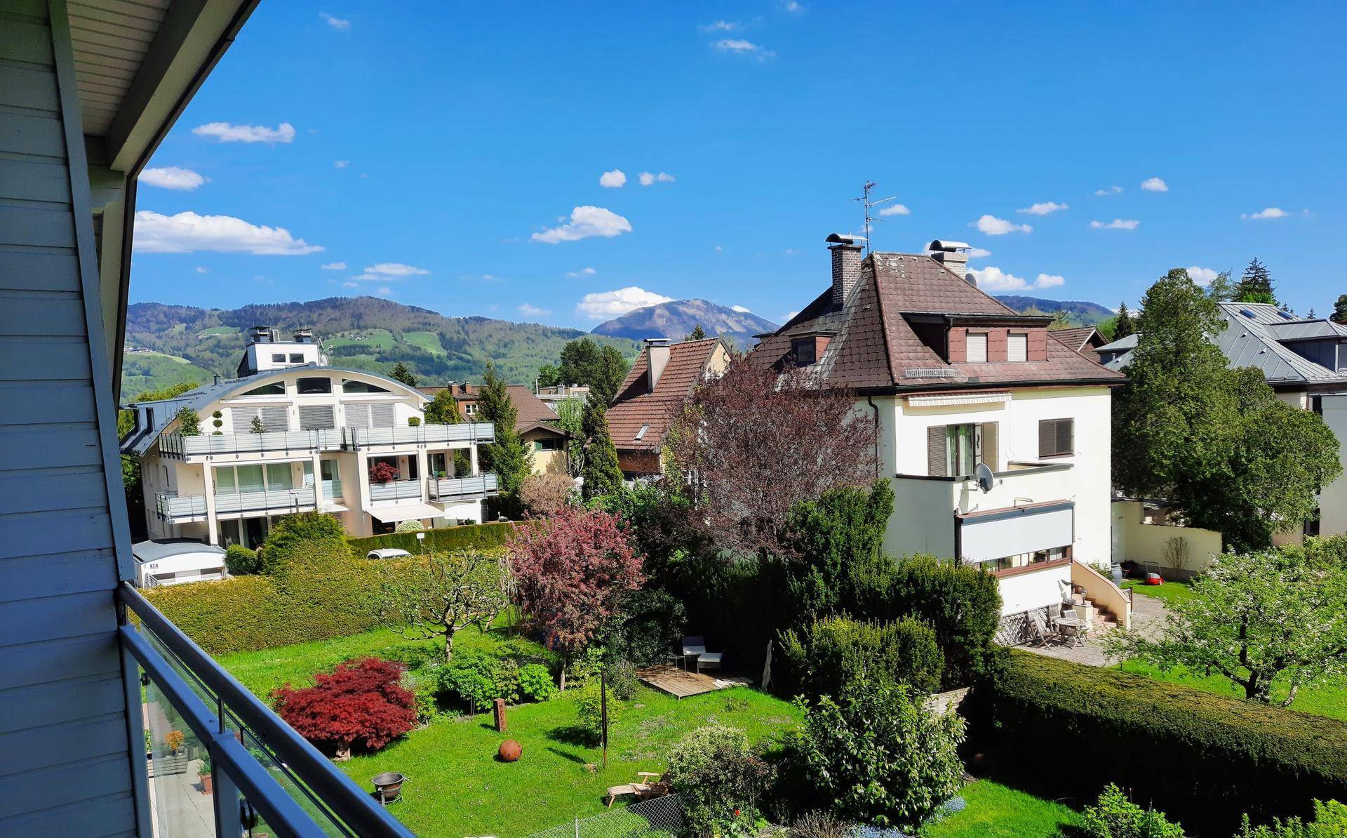 Weitläufiger Blick von einem Balkon über Gärten und Wohnhäuser bis zu den Bergen.