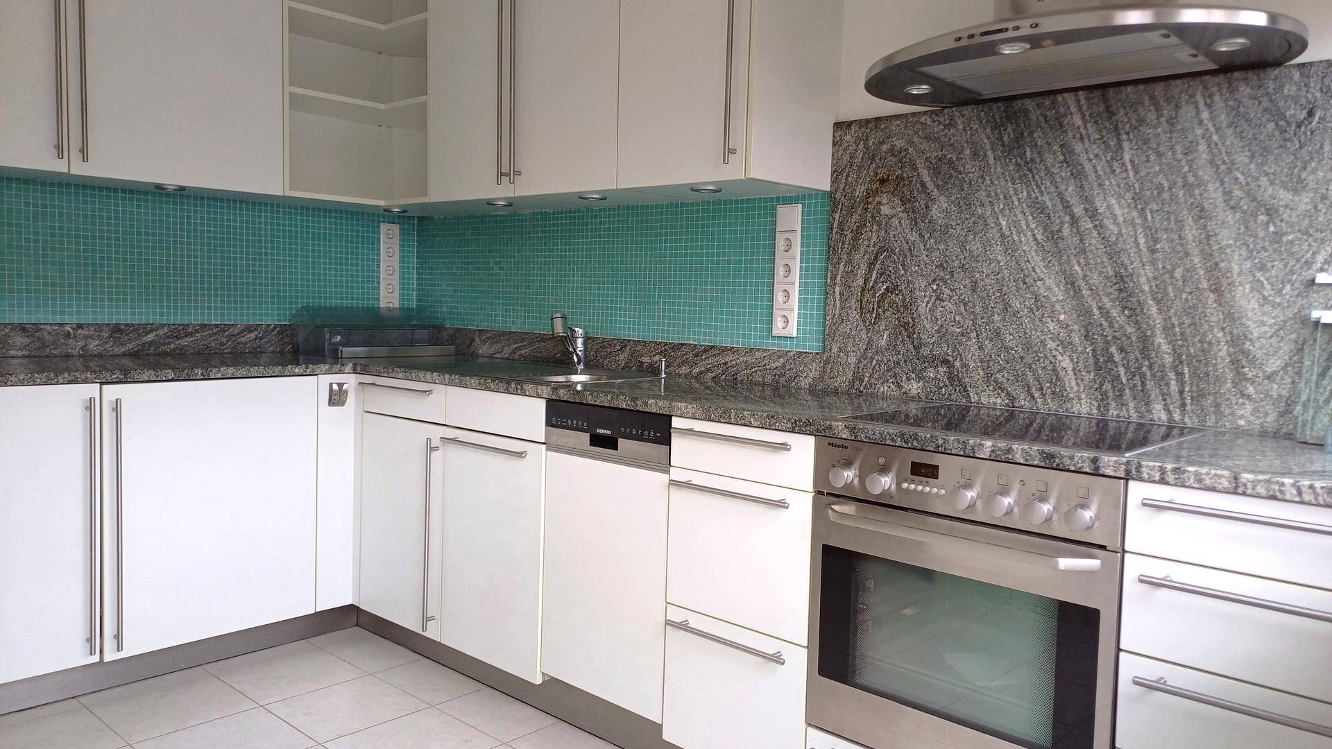 Moderne Küche mit weißen Schränken, Granitarbeitsplatte und türkisfarbenem Fliesenspiegel.