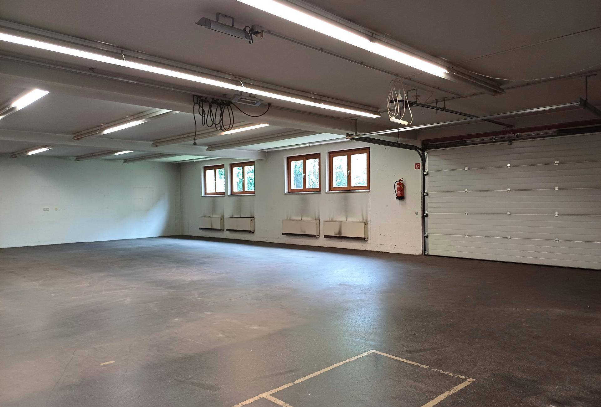 Geräumiger Lagerbereich mit Betonboden, großen Fenstern und industrieller Deckenbeleuchtung.
