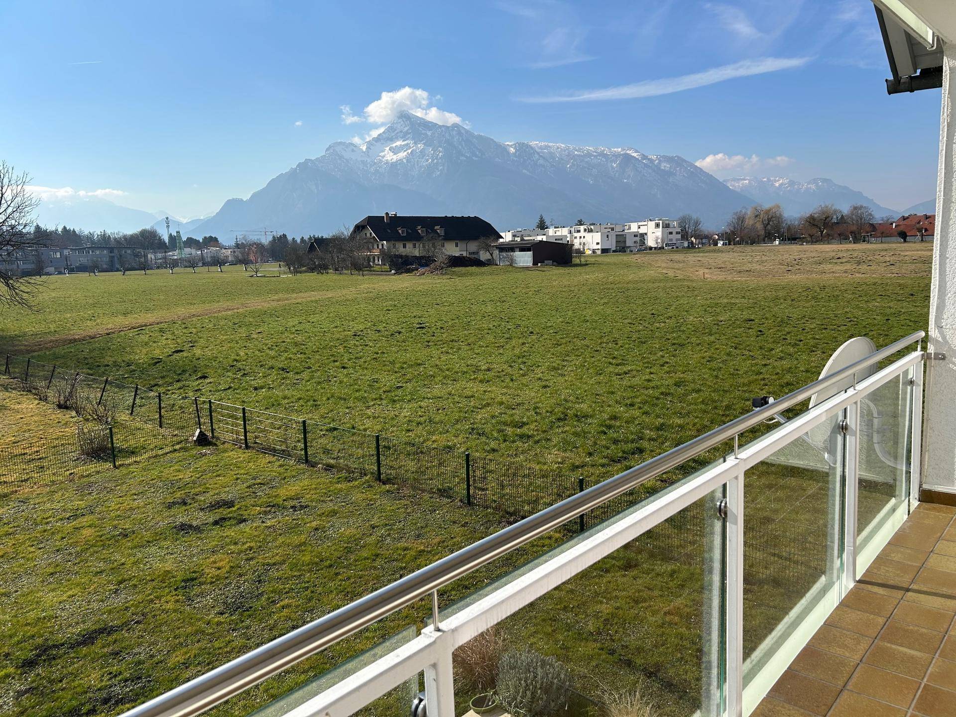 Sonniger Balkon mit weitem Blick über grüne Felder und schneebedeckte Berge.