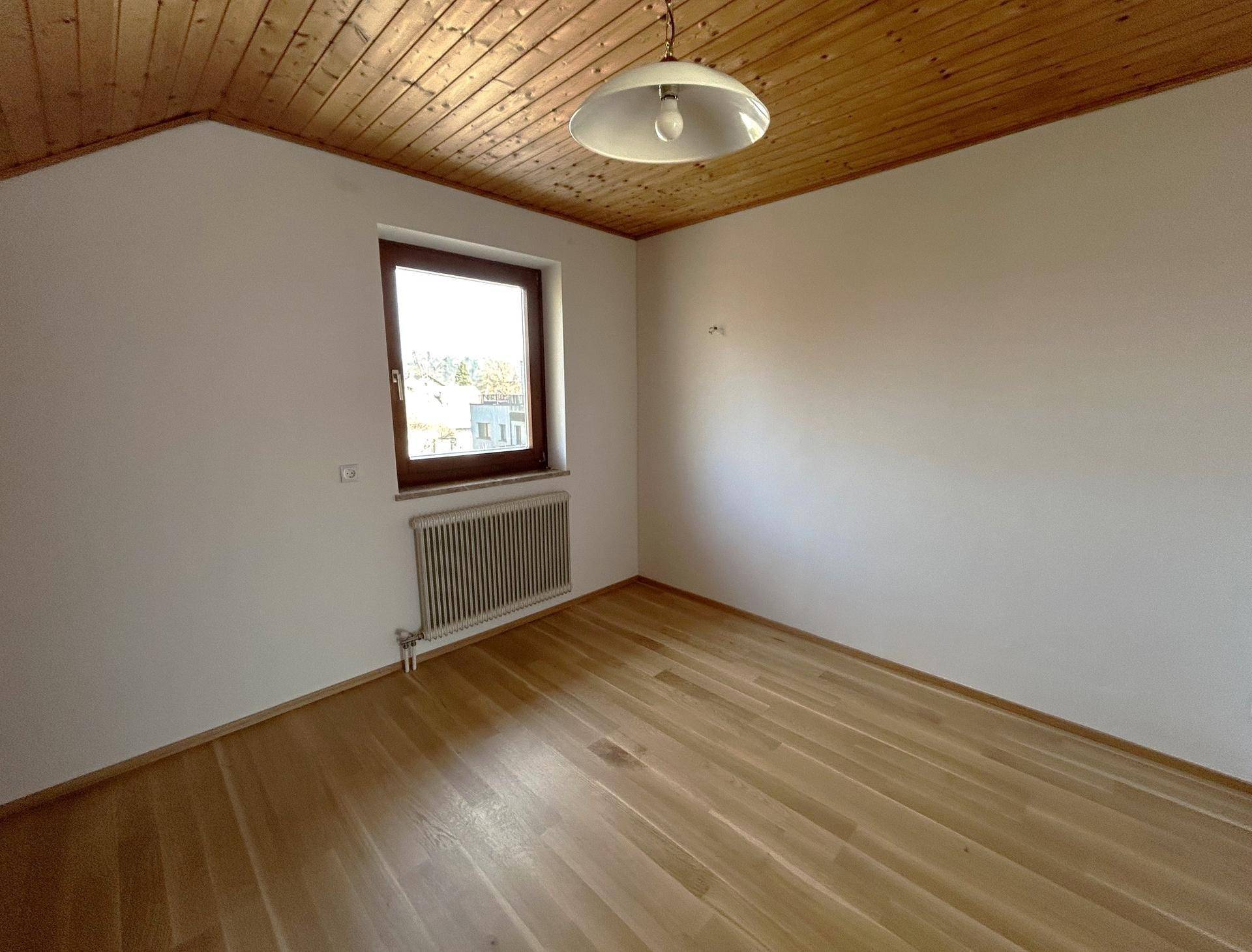 Helles Schlafzimmer im Dachgeschoss mit Holzdecke, Parkettboden und einem Fenster.