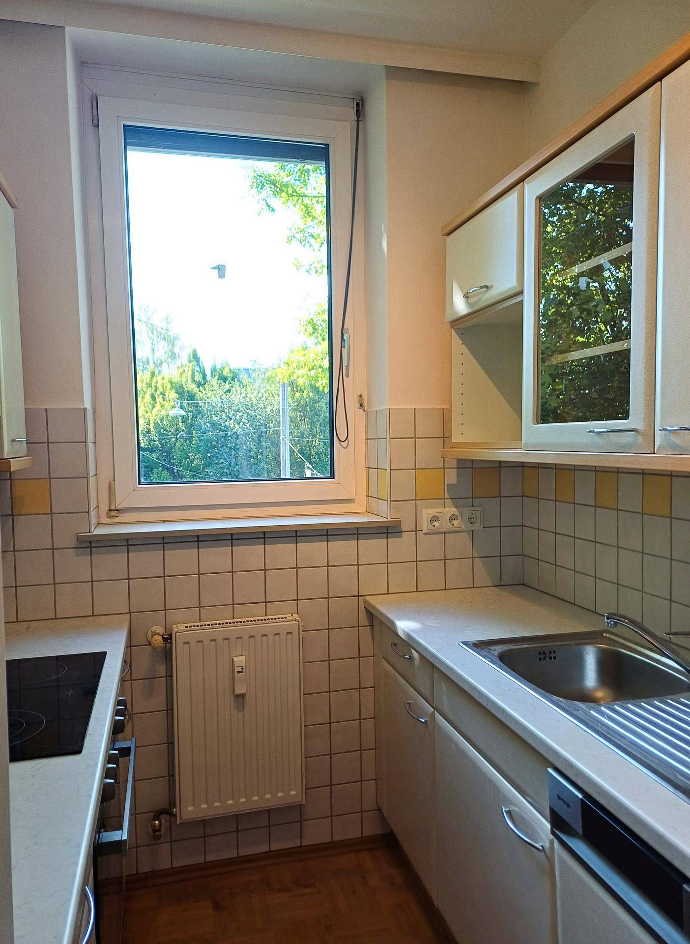 Küchenzeile mit Spüle, Fenster und gelb-weißen Fliesen, die einen Blick ins Grüne bietet.