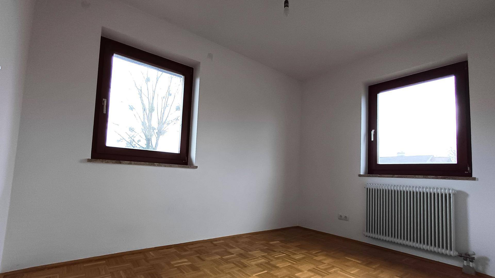 Schlafzimmer mit Parkettboden, weißen Wänden und zwei Fenstern für viel Tageslicht.