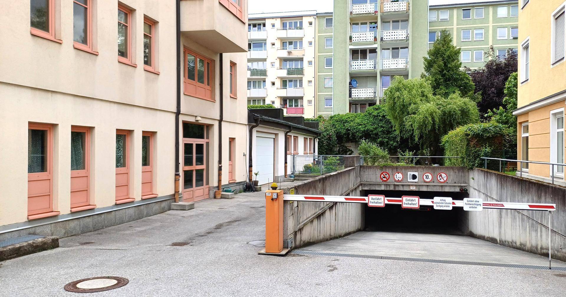 Außenansicht des Gebäudes mit Zufahrt zu einer Tiefgarage und umliegenden Wohngebäuden.