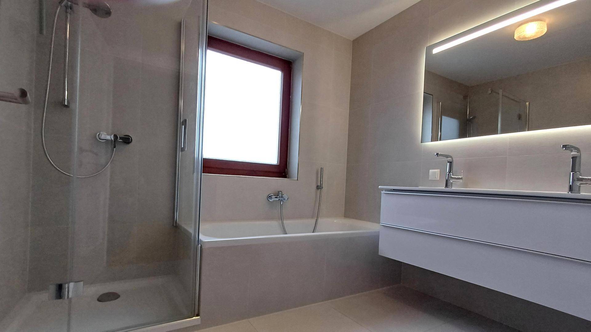 Modernes Badezimmer mit Doppelwaschbecken, Badewanne, Dusche und großen Fliesen.