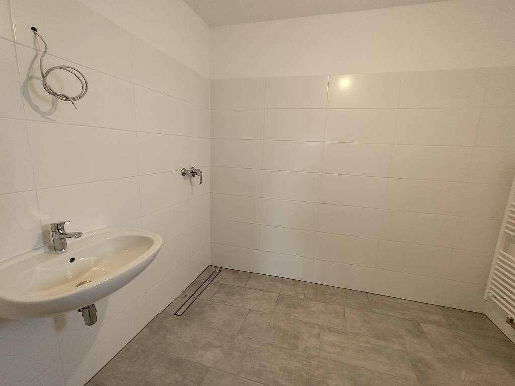 Modernes Badezimmer mit großformatigen Fliesen, Einzelwaschbecken und begehbarer Dusche.