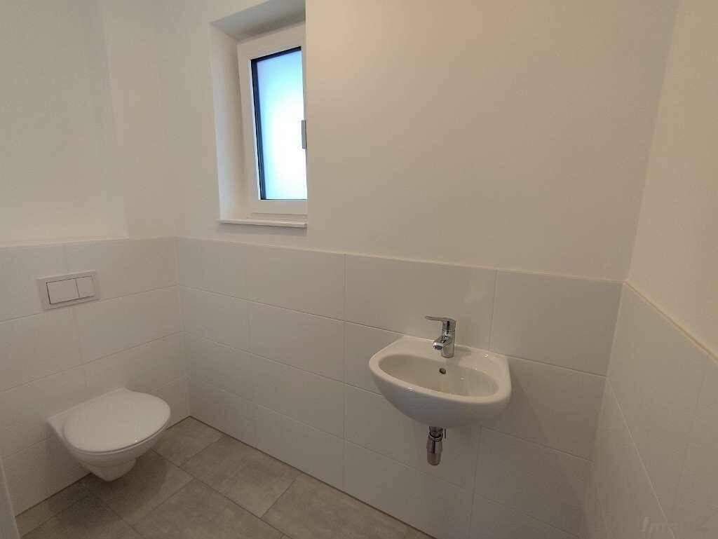 Helles Gäste-WC mit Fenster, wandhängender Toilette und kleinem Waschbecken.