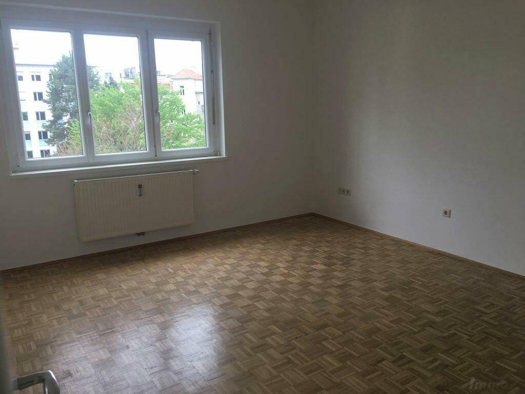 Helles Schlafzimmer mit Parkettboden und großem Fenster mit Blick ins Grüne.