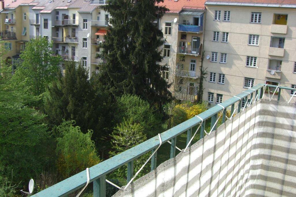 Aussicht von einem Balkon auf benachbarte Gebäude und üppiges Grün.