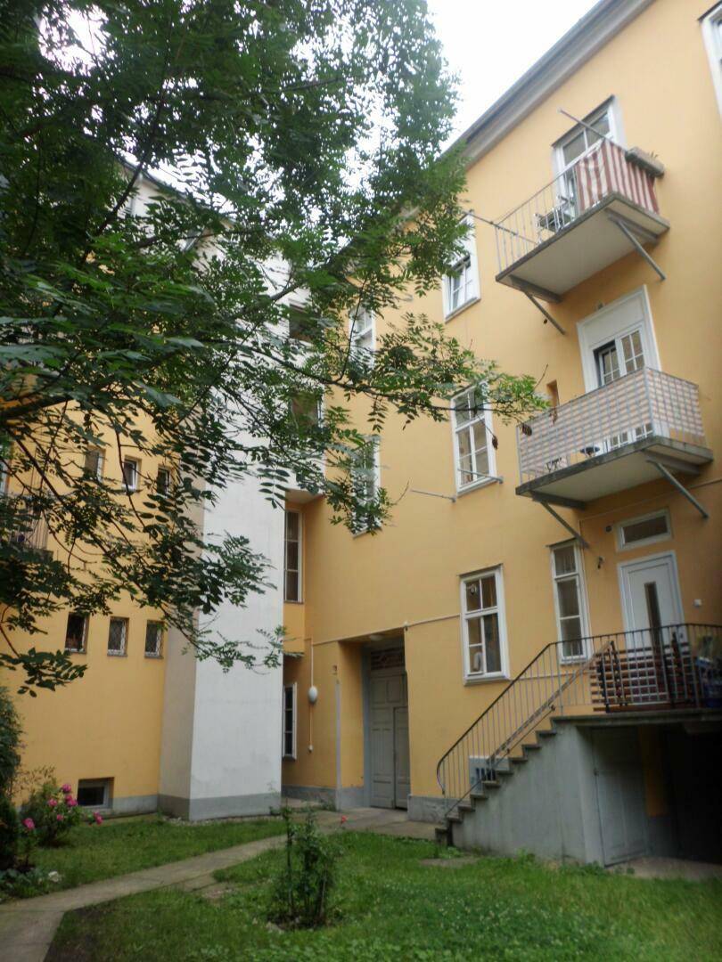 Innenhof eines Mehrfamilienhauses mit gelber Fassade, Balkonen und Grünflächen.