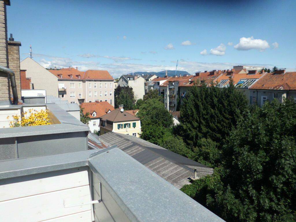 Weitblick von einem Balkon über die Dächer der Stadt und grüne Baumwipfel.