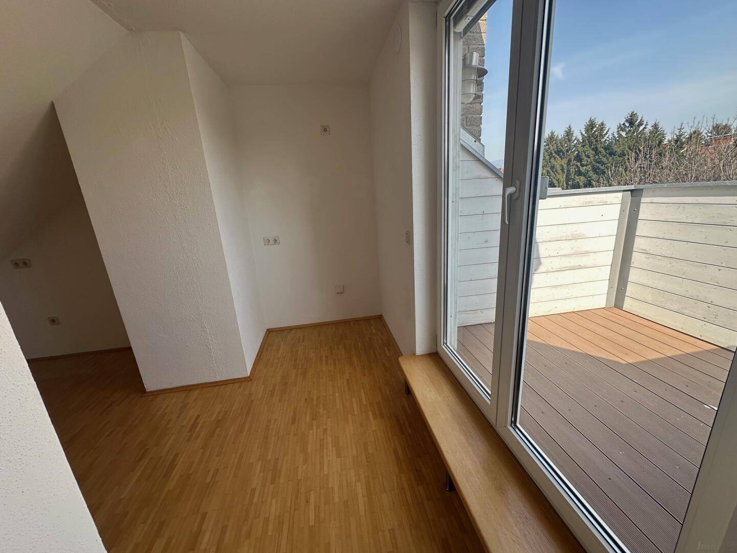 Heller Wohnraum mit Holzboden, Dachschrägen und Zugang zu einer Terrasse.