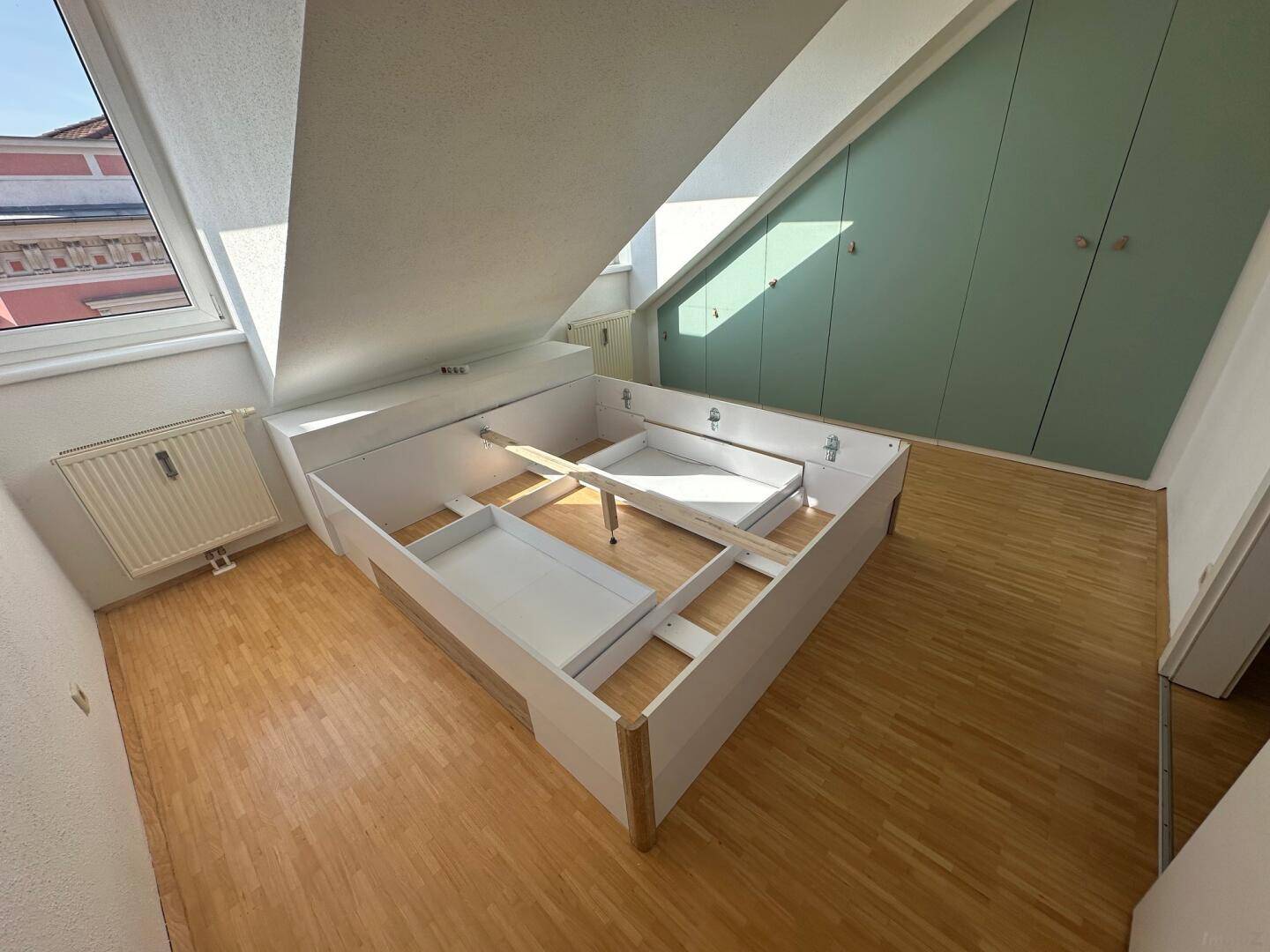 Helles Schlafzimmer mit Holzboden, Dachschrägen und Einbauschränken in Mintgrün.