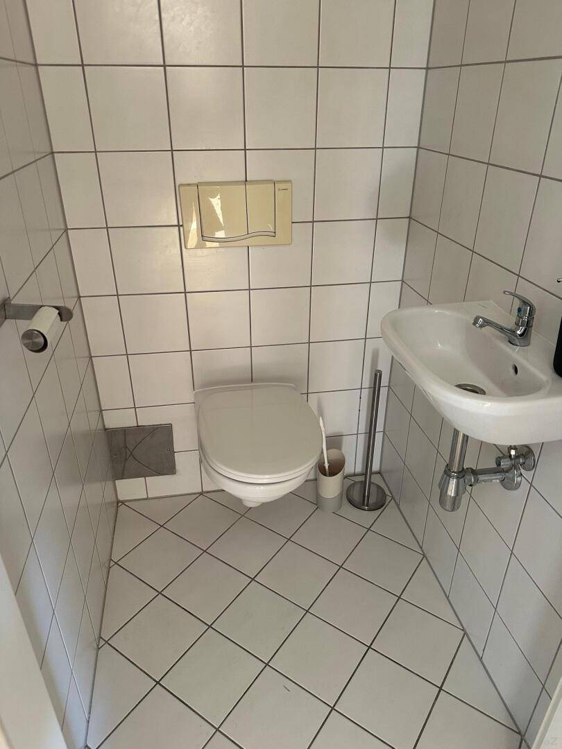 Kleines Gäste-WC mit Wand-WC, Waschbecken und weißen Fliesen.