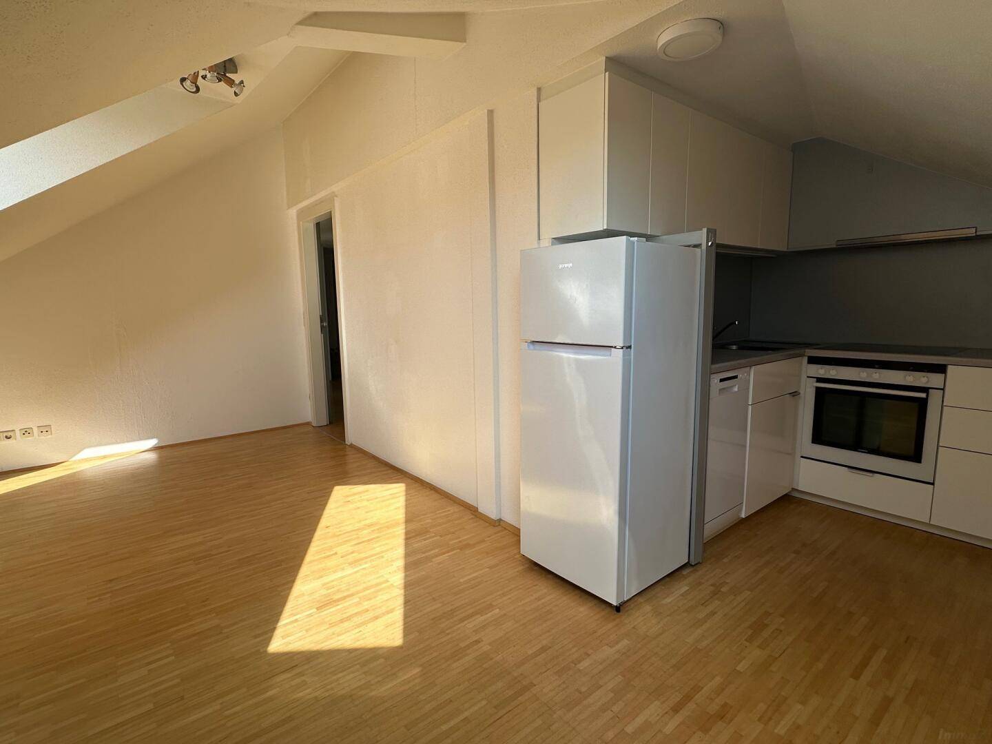 Kleine Küche mit weißen Schränken, Holzboden und Dachschräge, hell beleuchtet.