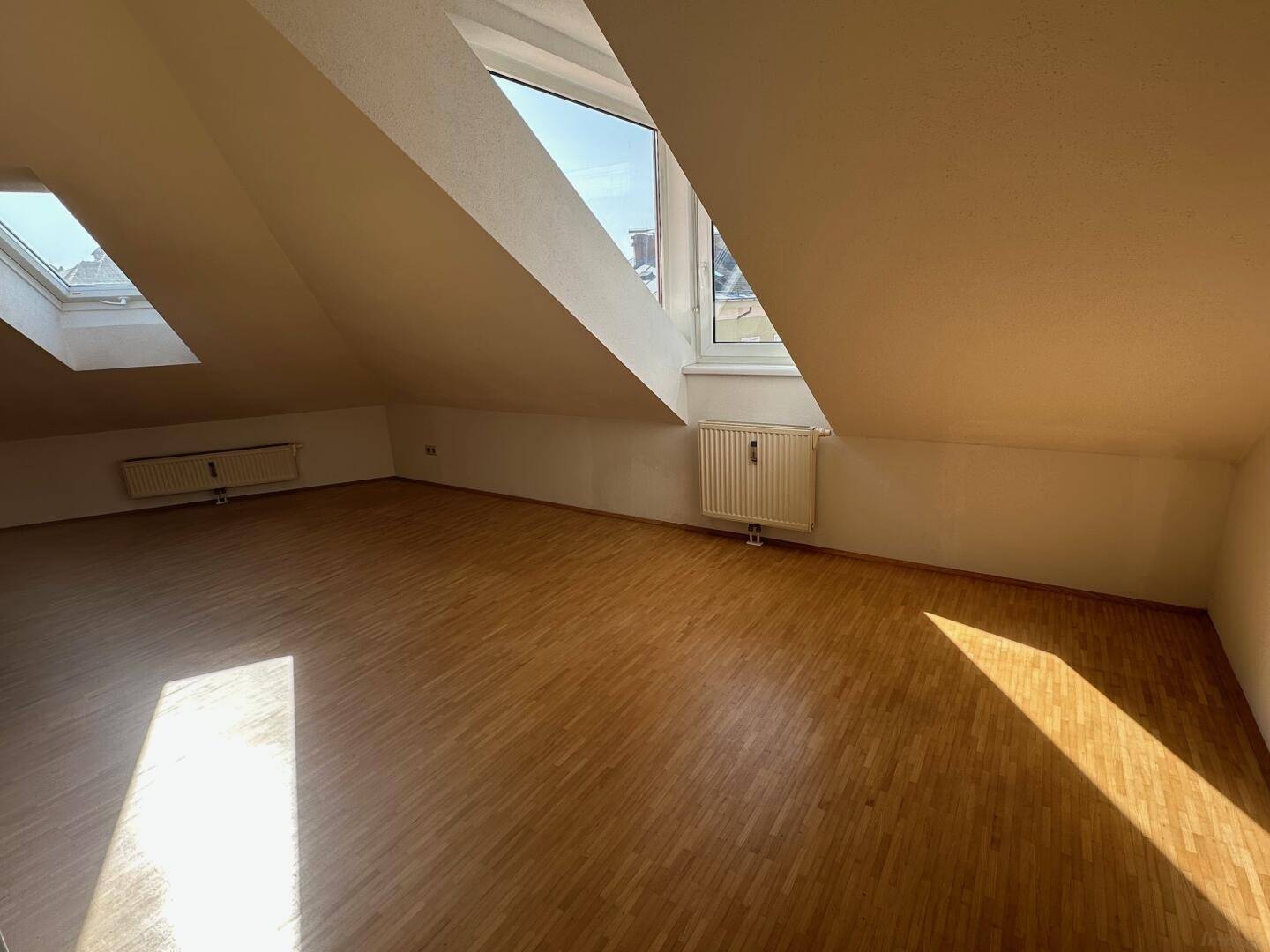 Heller Wohnraum mit Holzboden, Dachschrägen und großen Fenstern für viel Tageslicht.