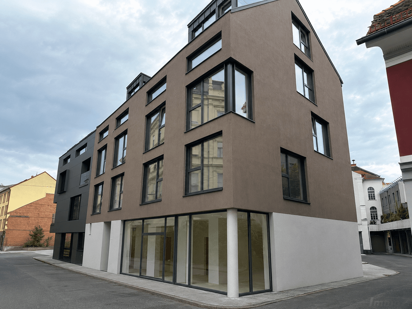 Moderne Architektur eines Neubaus mit brauner Fassade und großen, dunklen Fensterrahmen.