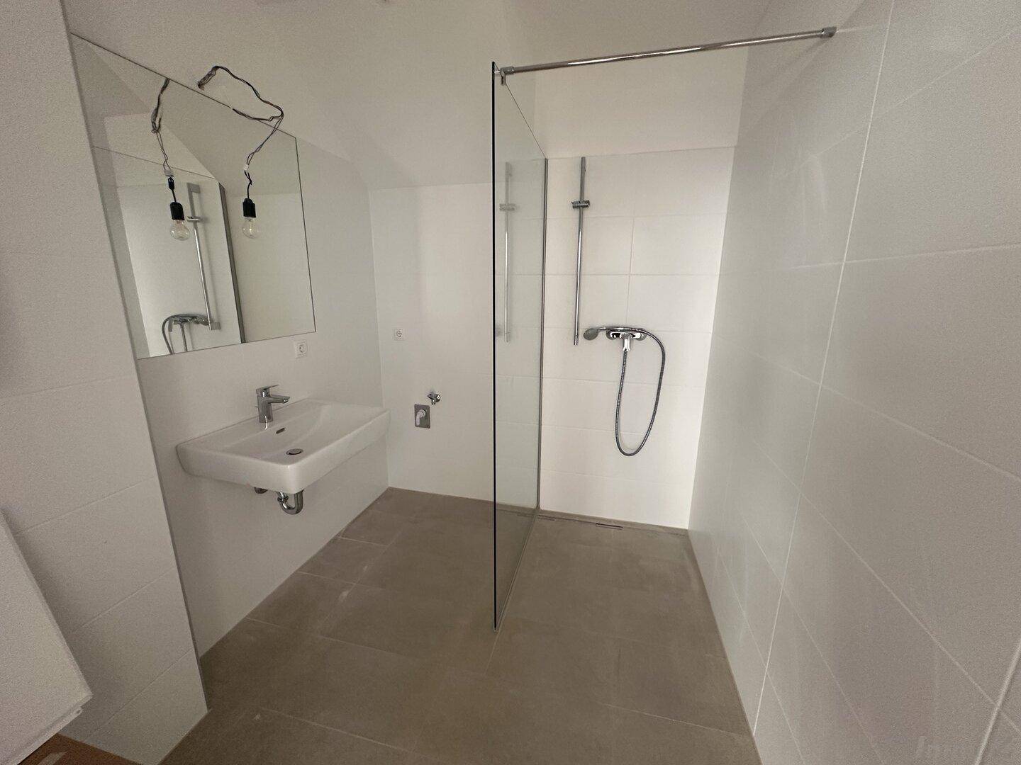 Modernes Badezimmer mit weißen Fliesen, wandmontiertem Waschbecken und begehbarer Dusche.
