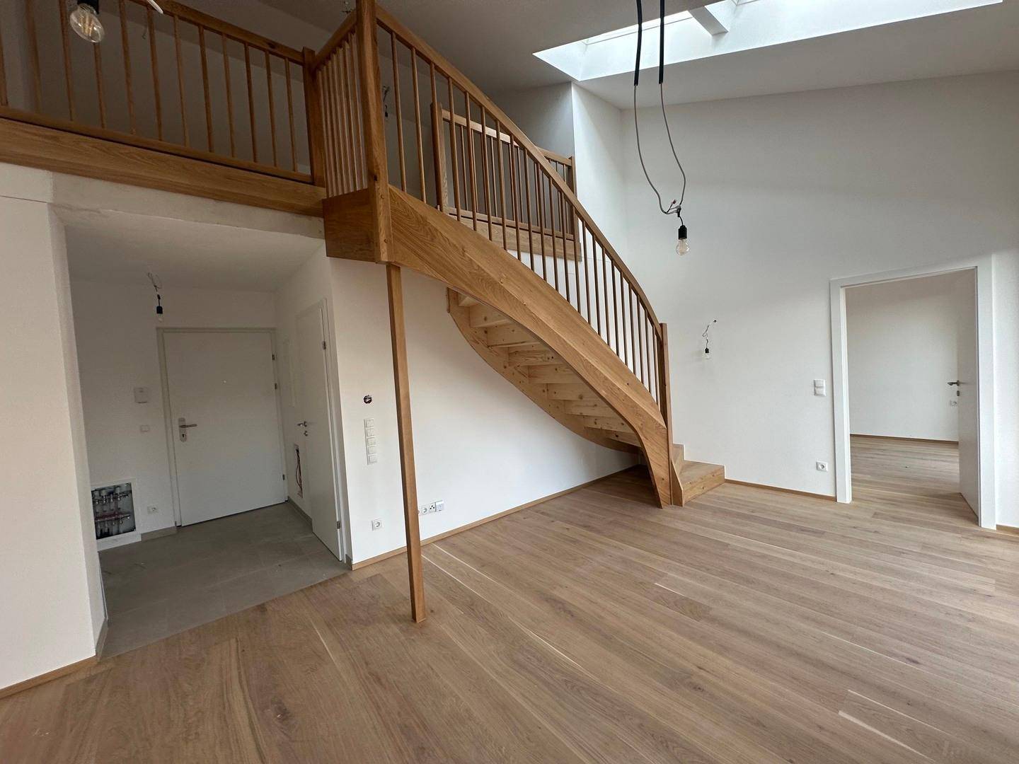 Heller Wohnbereich mit eleganter Holztreppe, hohen Decken und natürlichem Licht durch ein Oberlicht.