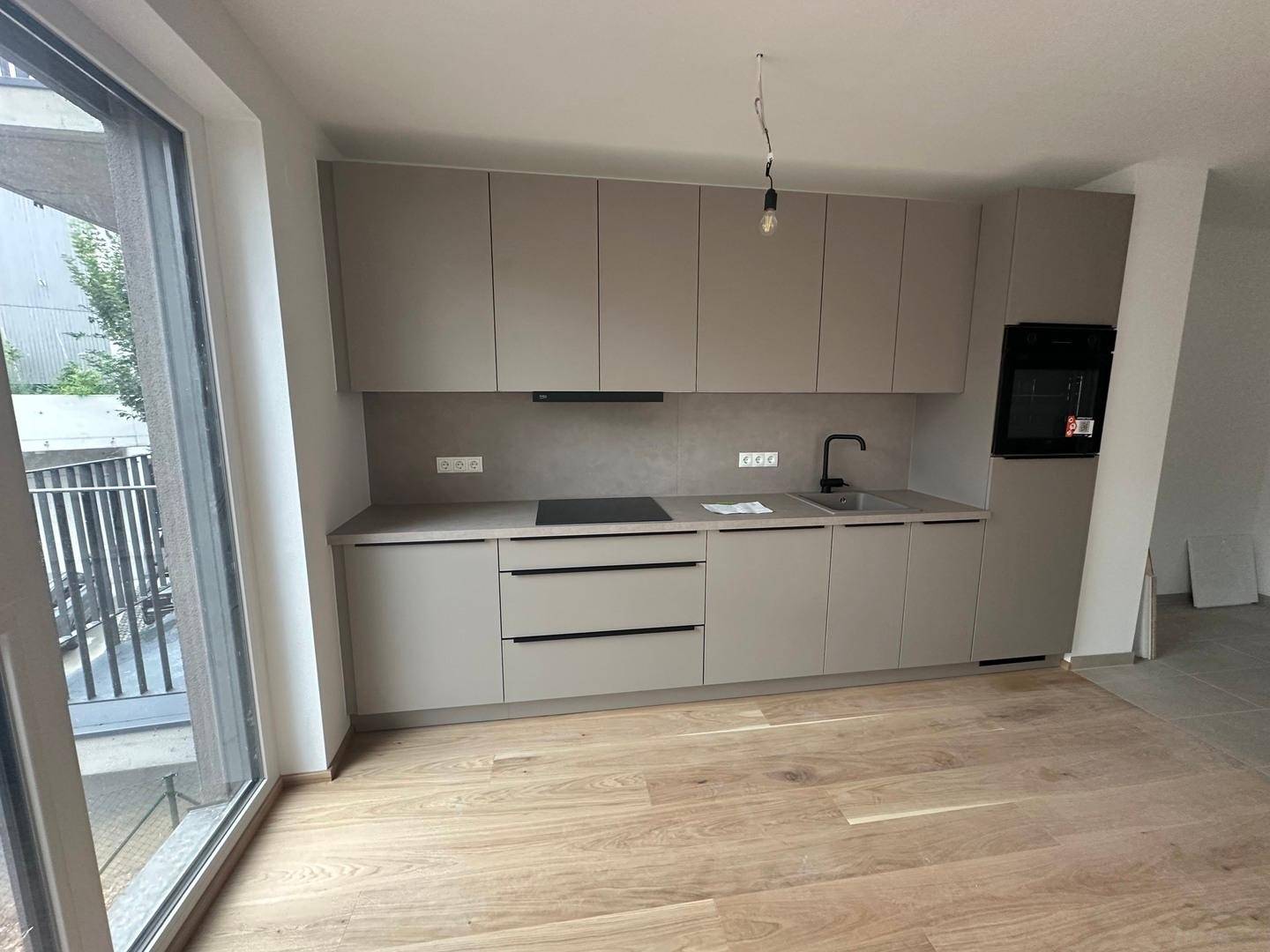 Moderne Küche mit hellgrauen Schränken, Induktionskochfeld und hellem Holzfußboden.