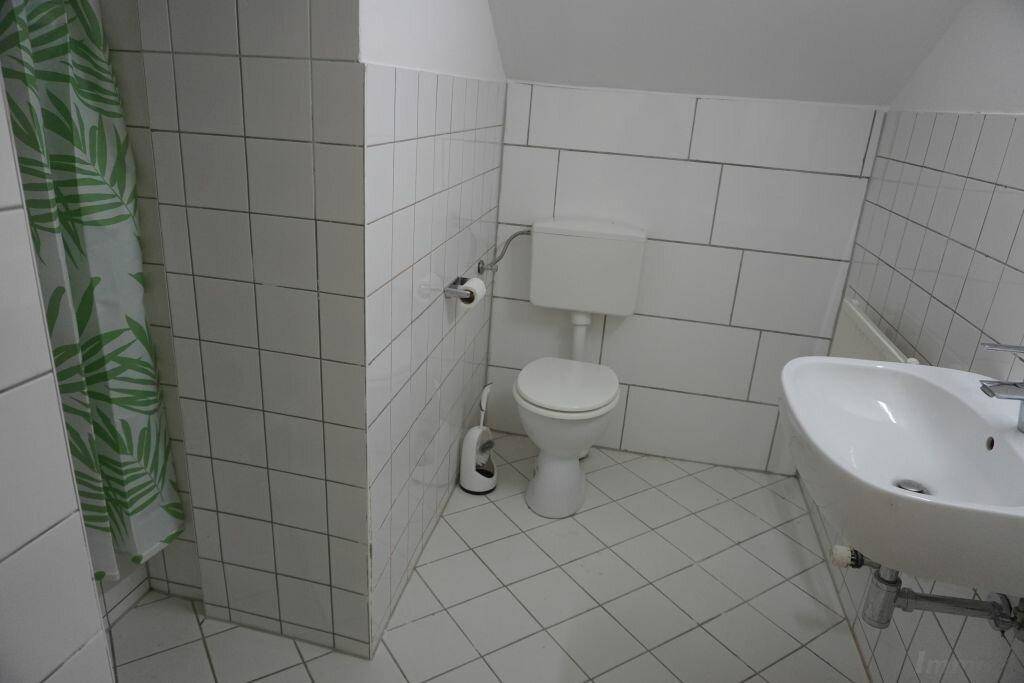 Badezimmer mit weißen Fliesen, Toilette, Waschbecken und Duschbereich mit Vorhang, sauber und hell.