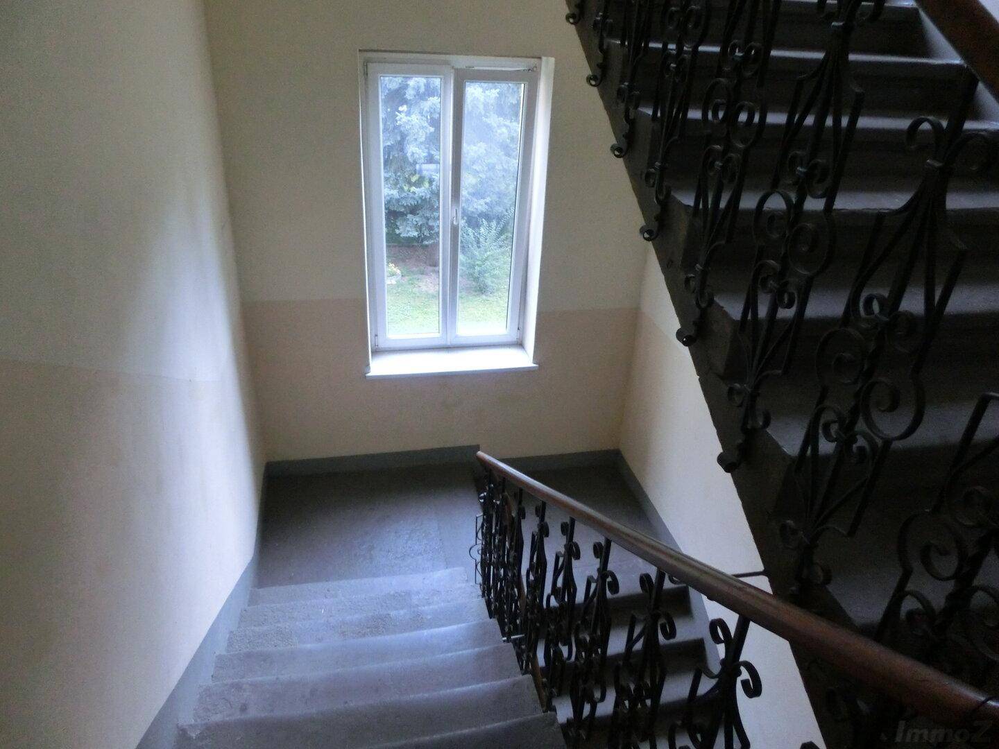 Treppenhaus mit schmiedeeisernem Geländer und einem Fenster, das natürliches Licht hereinlässt.