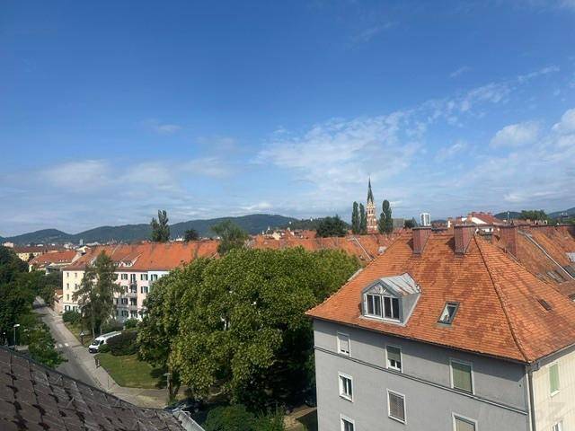 Weitläufiger Blick über die Stadt mit roten Dächern und Bergen im Hintergrund.