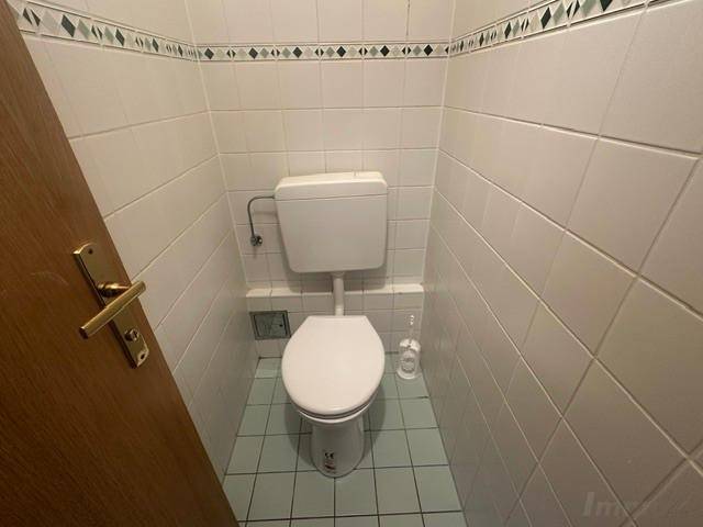 Kleines Gäste-WC mit weißen Fliesen und Toilette.