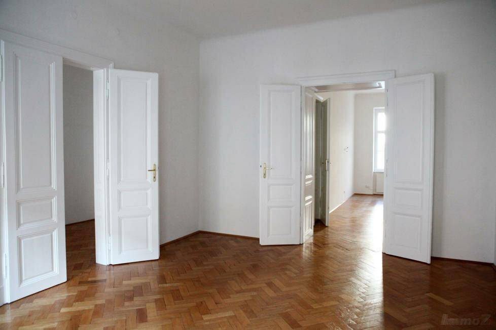 Leerer Raum mit glänzendem Fischgrätparkett und hohen weißen Flügeltüren.